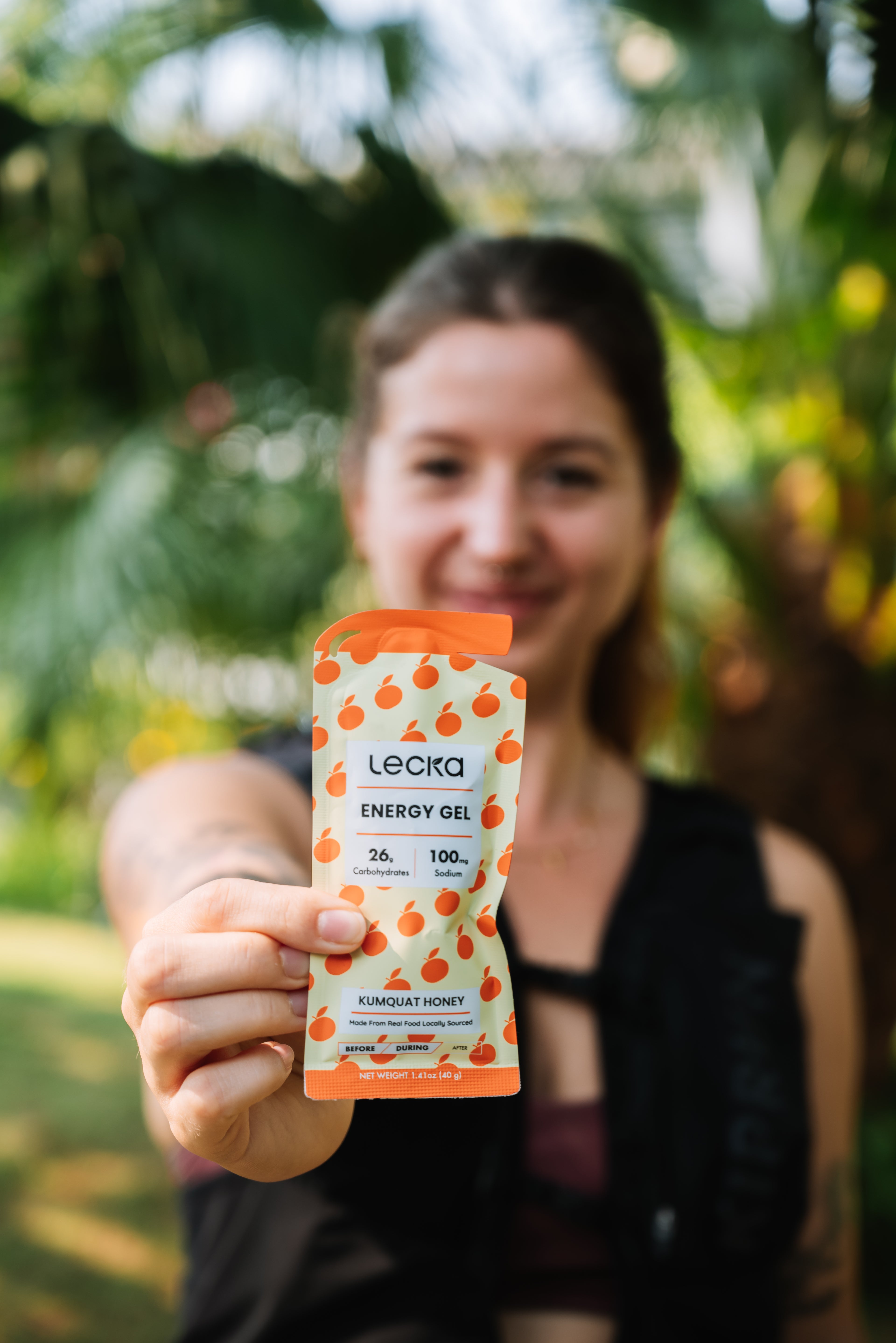 Person holding a Lecka energy gel package outdoors with greenery in the background