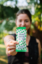 Person holding a Leela energy gel package outdoors with greenery in the background