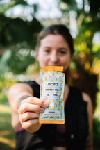 Person holding a Lecka energy gel package outdoors with greenery in the background