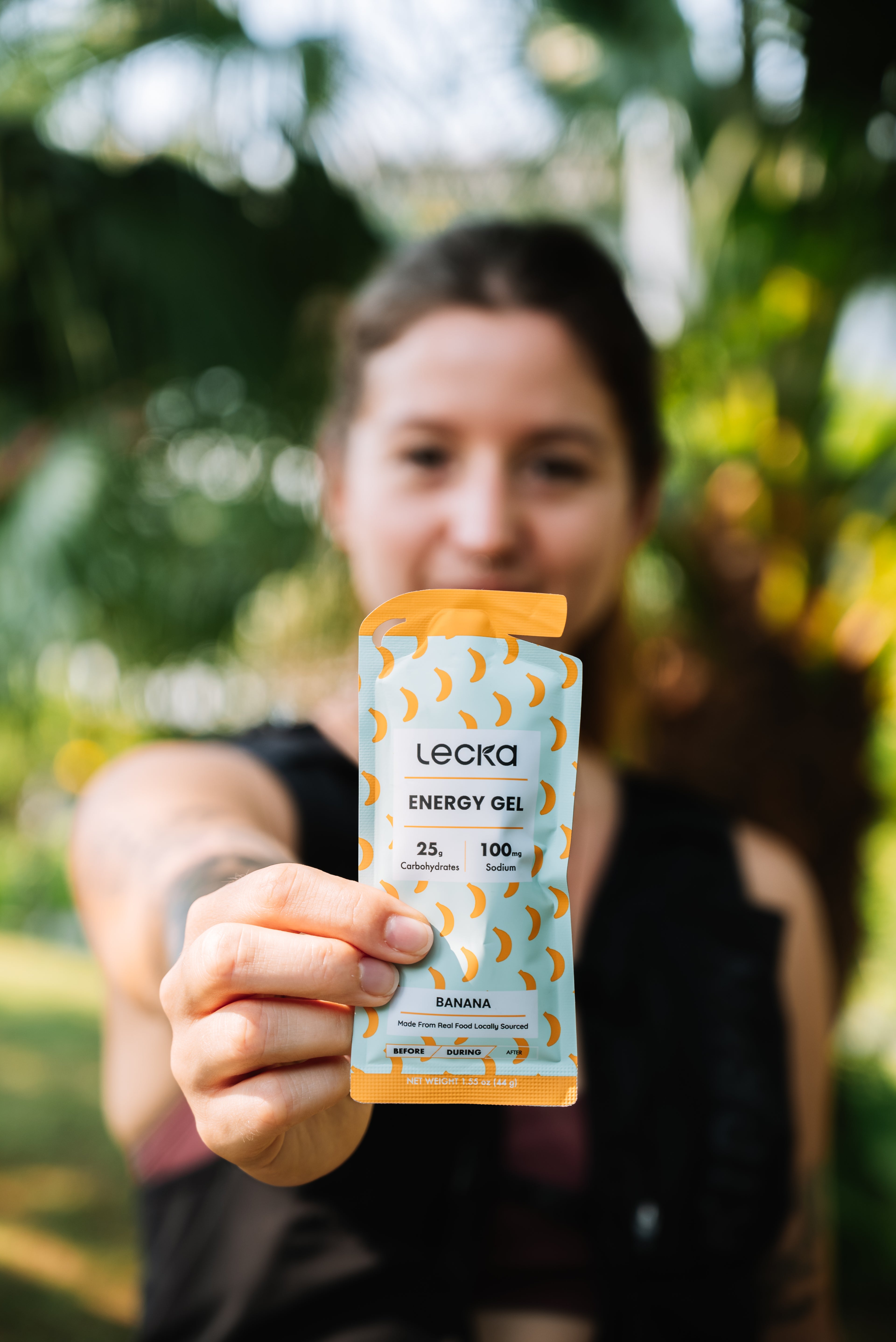 Person holding a Lecka energy gel package outdoors with greenery in the background